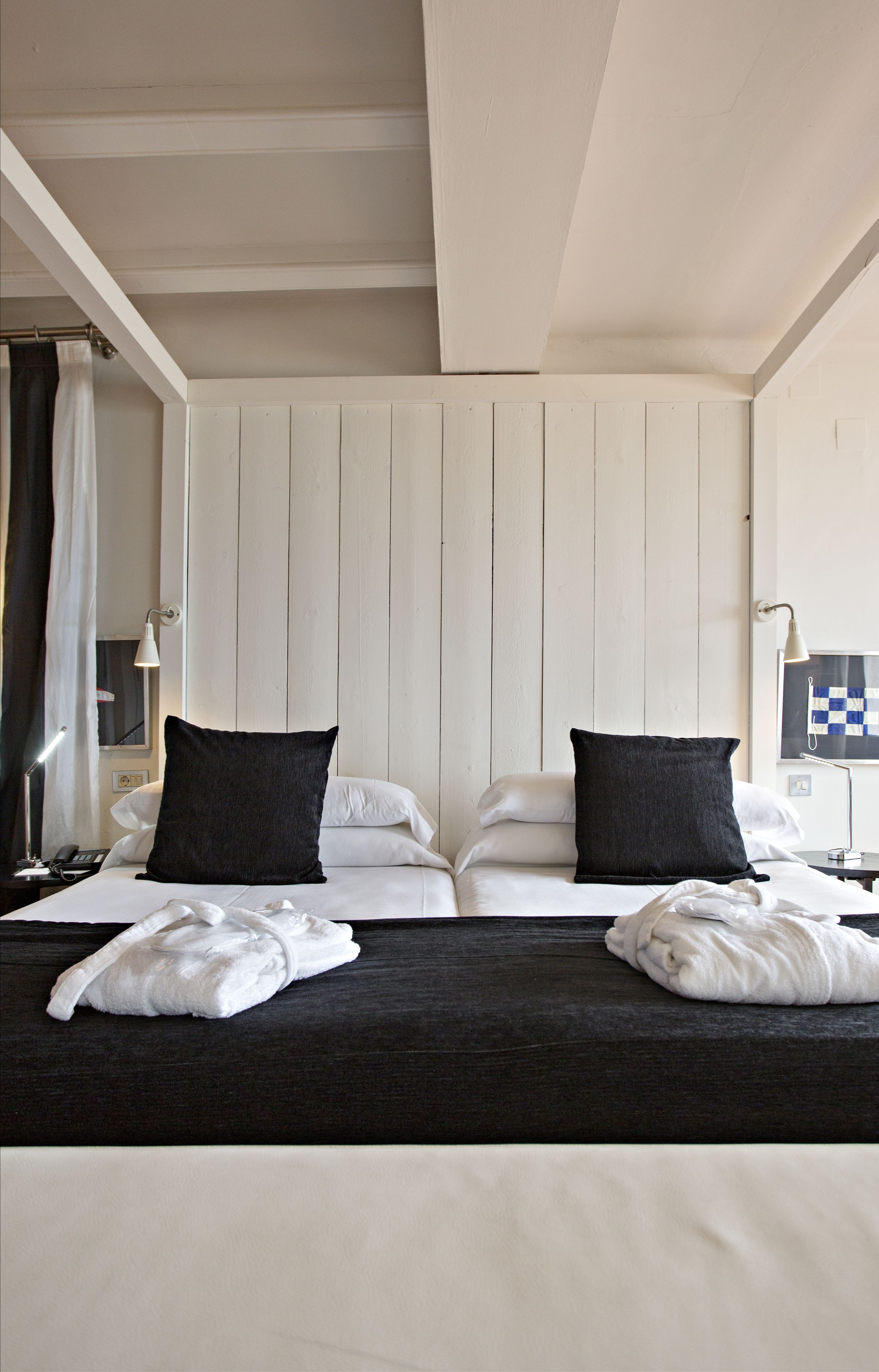 Habitación de hotel con cama, dos almohadas, una mesita de noche, una lámpara y una pared con bandera a cuadros.