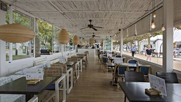 An indoor dining area with wooden tables and chairs, ceiling fans, and large windows.