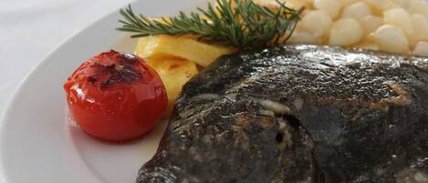 Ein Teller mit gegrilltem Fisch, gerösteter Tomate und gekochten Kartoffeln.