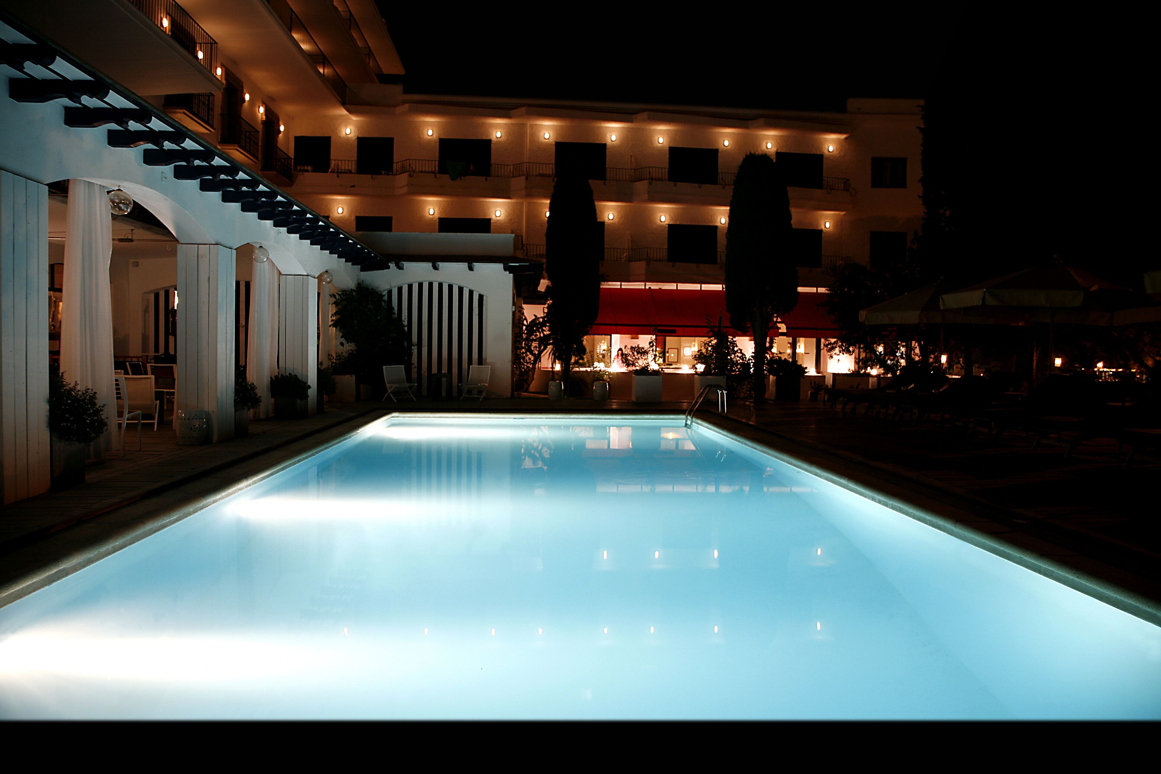 Une piscine dont le bord est illuminé, un escalier et un bâtiment avec de nombreux balcons en arrière-plan.