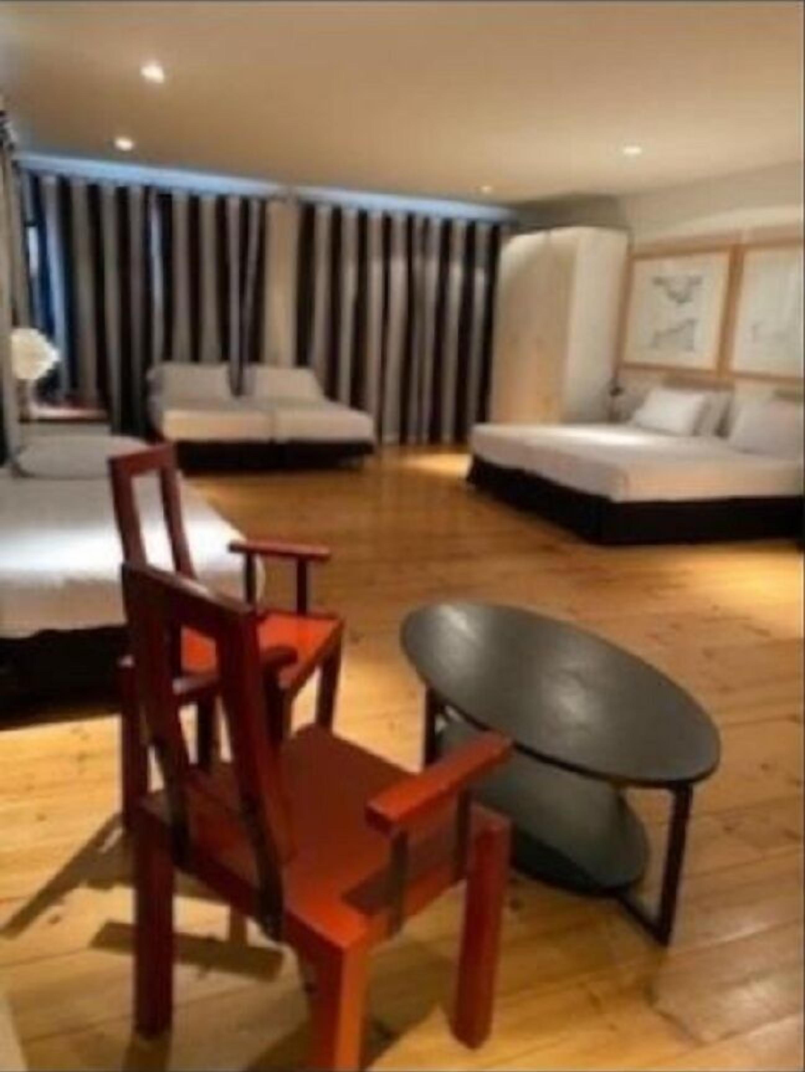 A modern living room with a wooden floor, a sofa, a chair, and a large black ottoman.