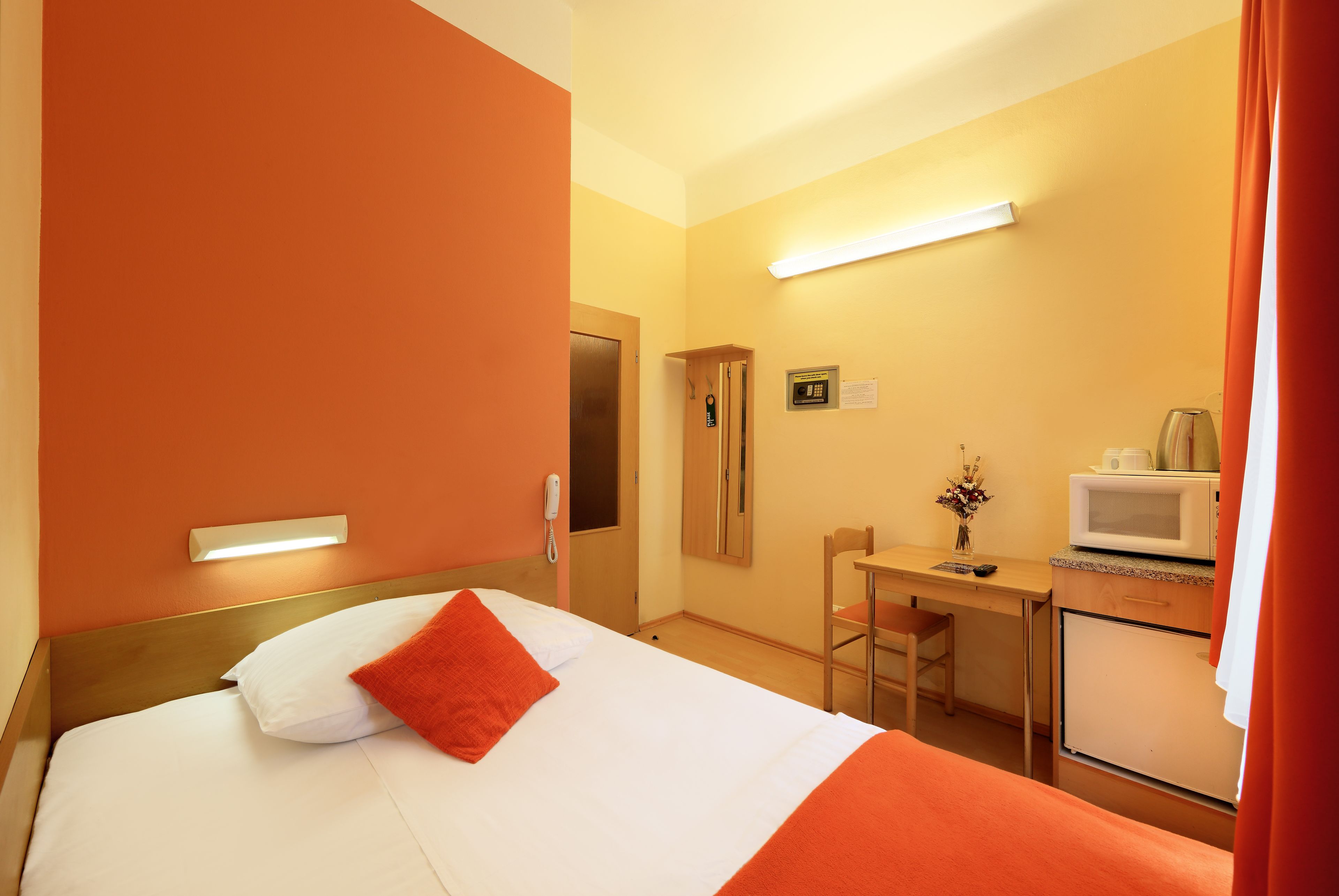 A hotel room with a bed, a desk, a microwave, and a small refrigerator.