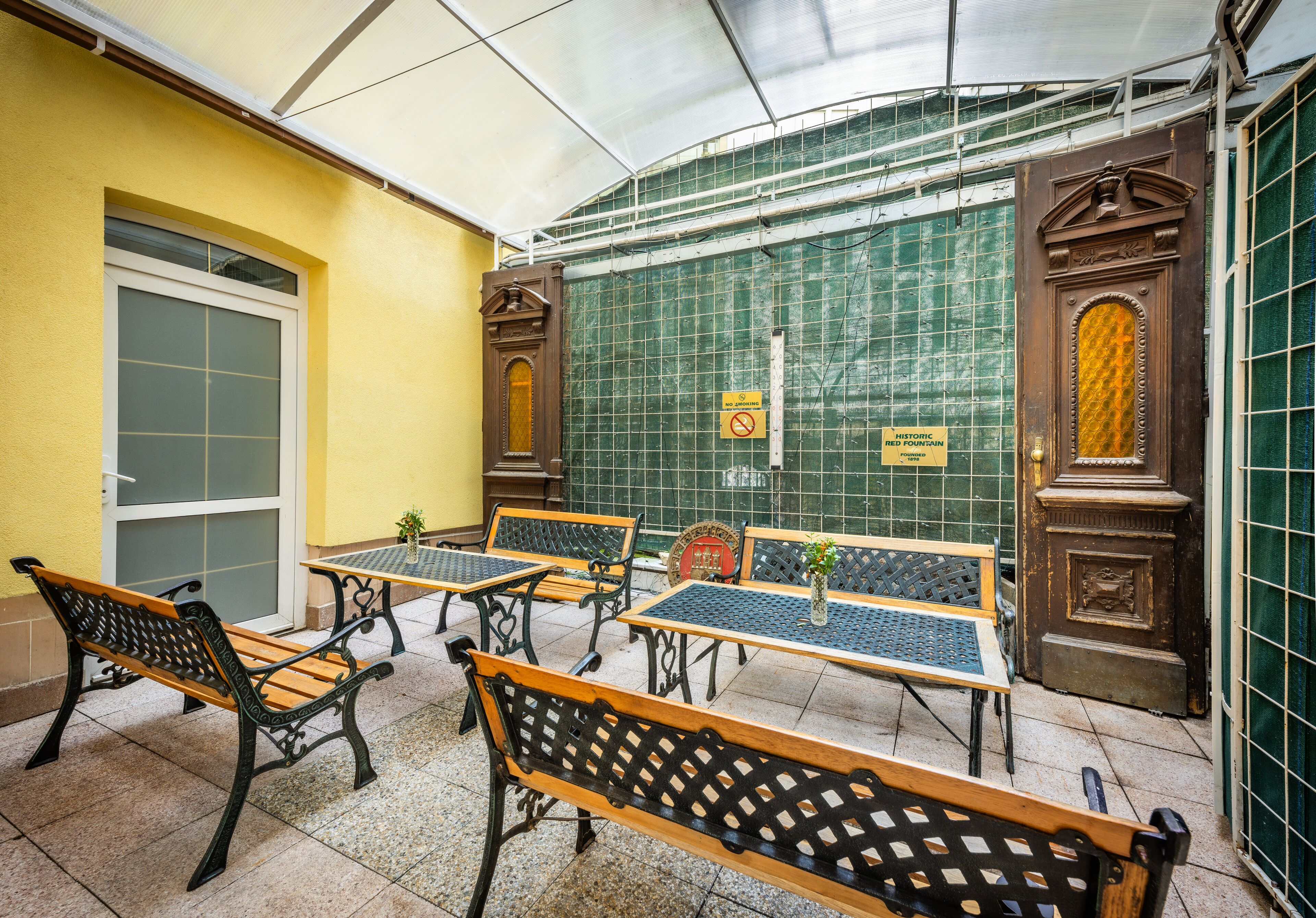 A covered outdoor seating area with tables and benches, a door, and a green wall with a sign.