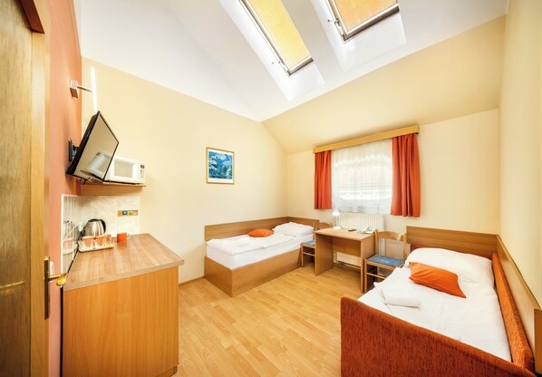 A compact hotel room with two beds, a desk, a chair, a microwave, and a small kitchenette. - Hotel Residence Tabor (Prague)