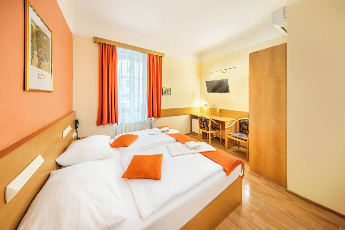 A hotel room with two beds, a desk, a chair, a TV, and a window with curtains.