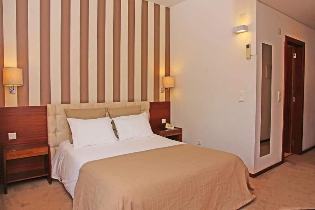 A hotel room with a large bed, two bedside tables, a wooden headboard, and a striped wall.