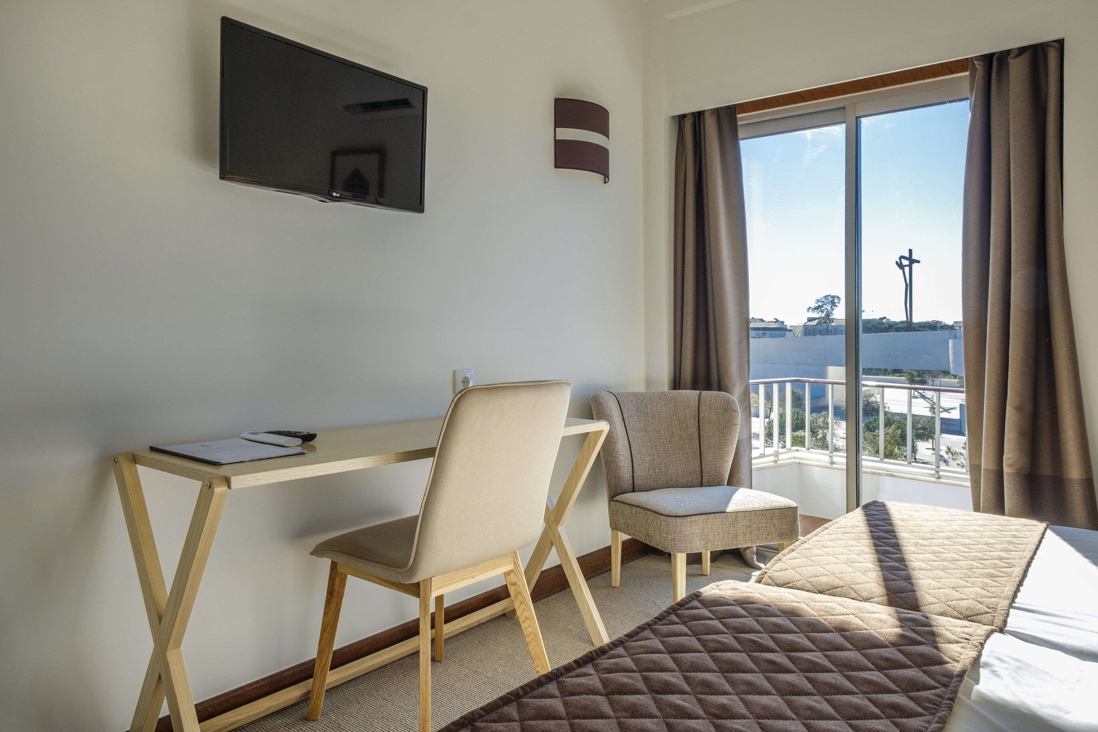 A hotel room with a bed, a desk, two chairs, a TV, and a balcony with a view.