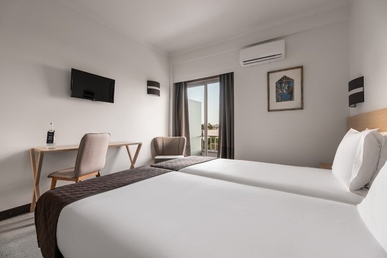 Habitación de hotel con una cama grande, un escritorio con una silla, un televisor montado en la pared y un equipo de aire acondicionado.