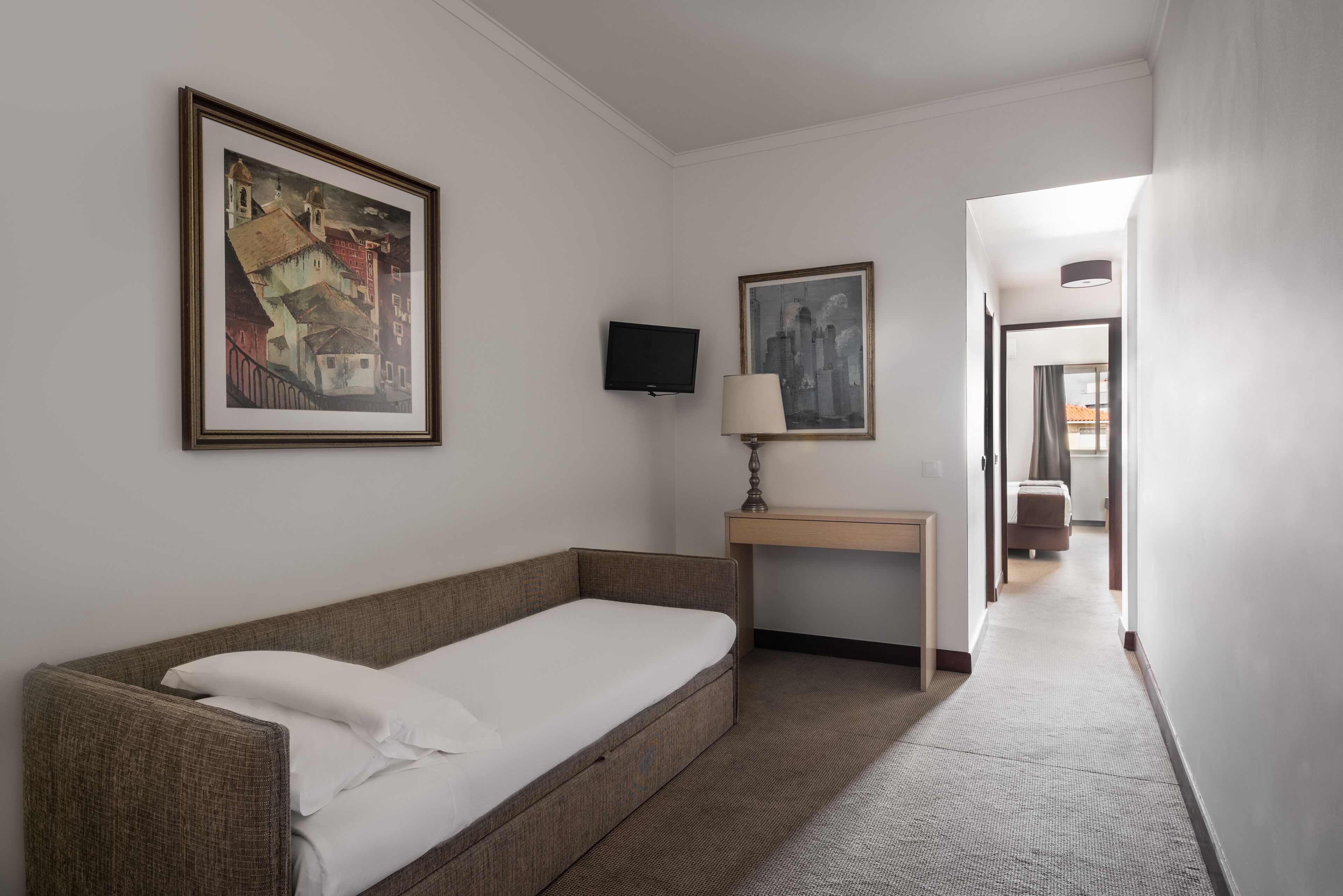 Hotelkamer met een éénpersoonsbed, een bureau met lamp, een flatscreen-tv en twee ingelijste kunstwerken aan de muur.