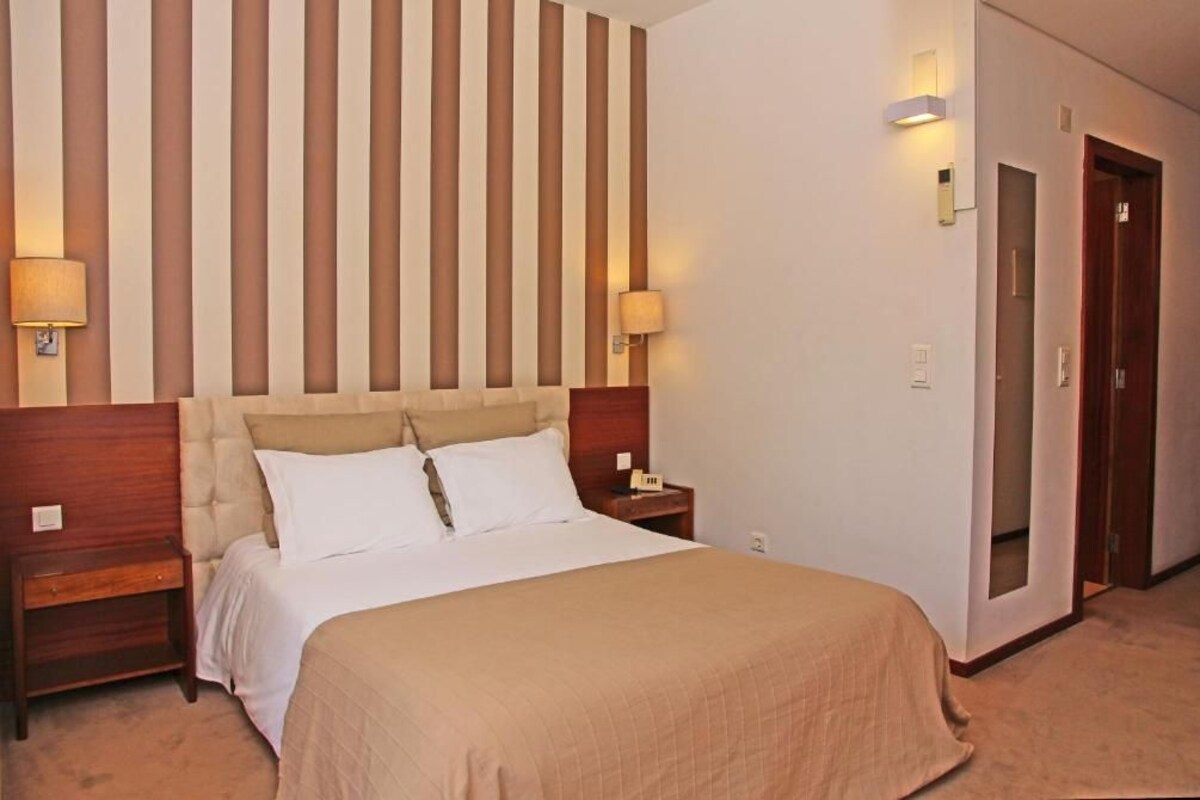 Habitación de hotel con una cama grande, dos mesitas de noche, un cabecero de madera y una pared a rayas.