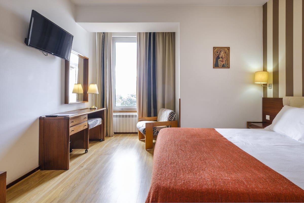 A hotel room with a bed, a desk, a chair, a television, and a window with curtains.
