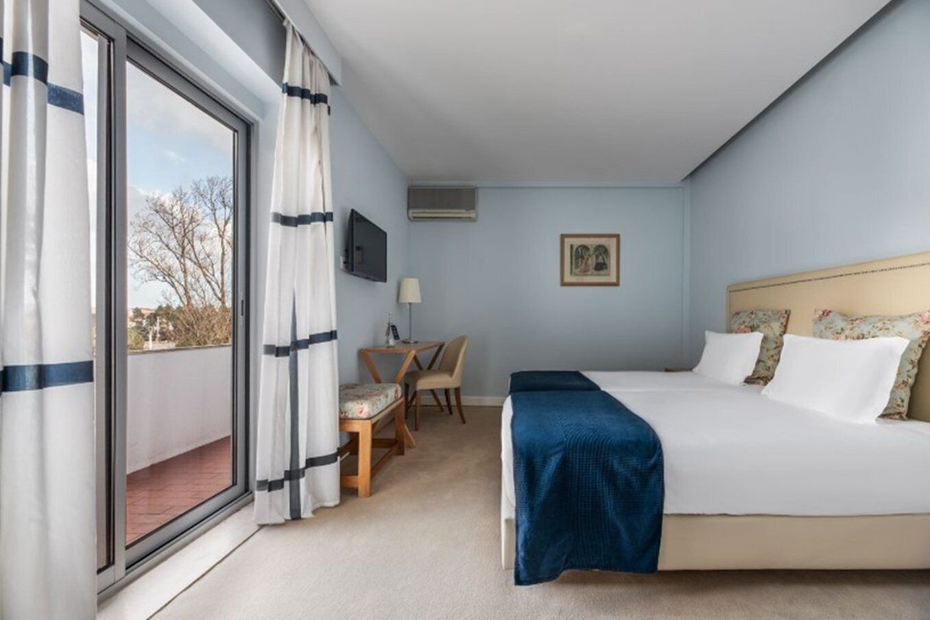 Habitación de hotel con cama, escritorio, silla, televisor y ventana con cortinas.