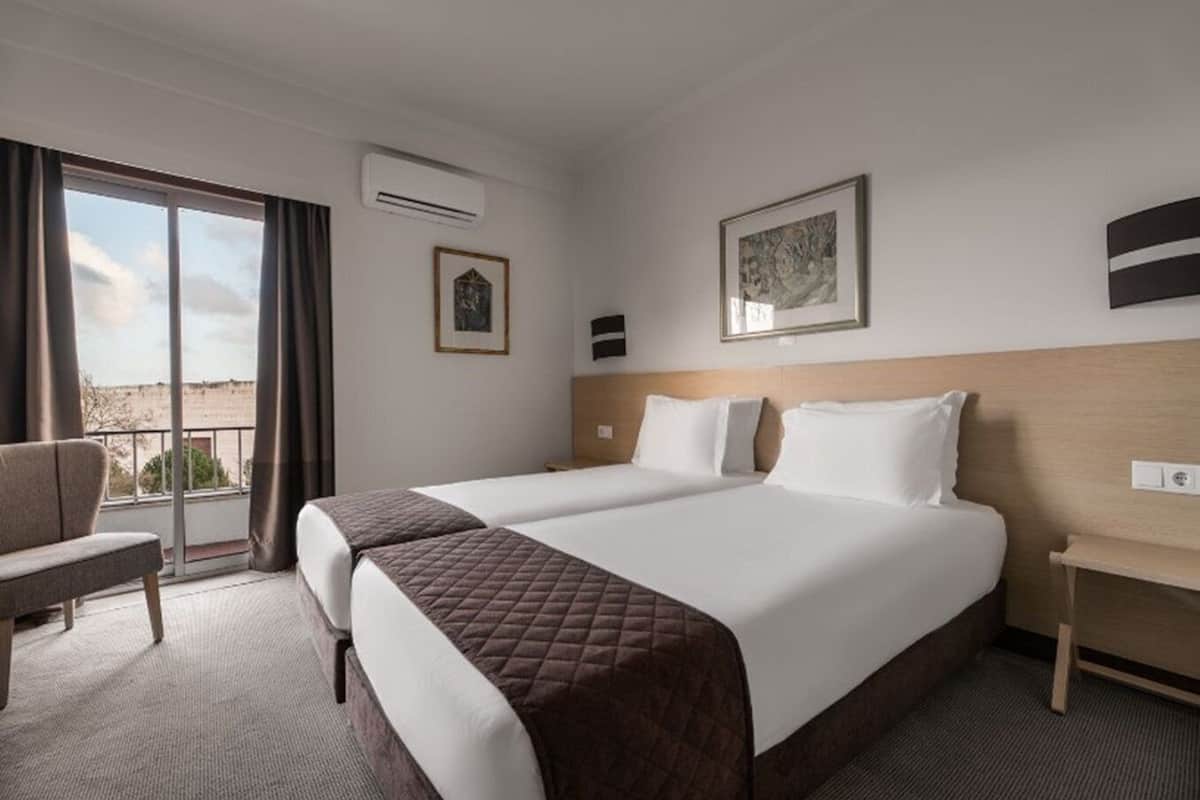 A hotel room with a large bed, a chair, a desk, and a view of the outdoors.