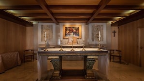 An altar with candles, a framed painting, and a cross on the wall. - Crisol Tres Pastorinhos (Ourem)