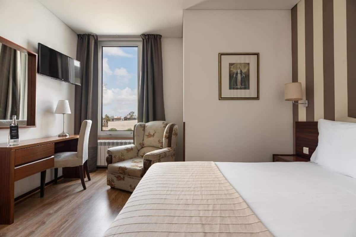 A hotel room with a bed, a desk, a chair, a TV, and a window with curtains.