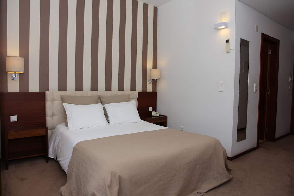A hotel room with a large bed, two bedside tables with lamps, a wooden headboard, and a striped wall.