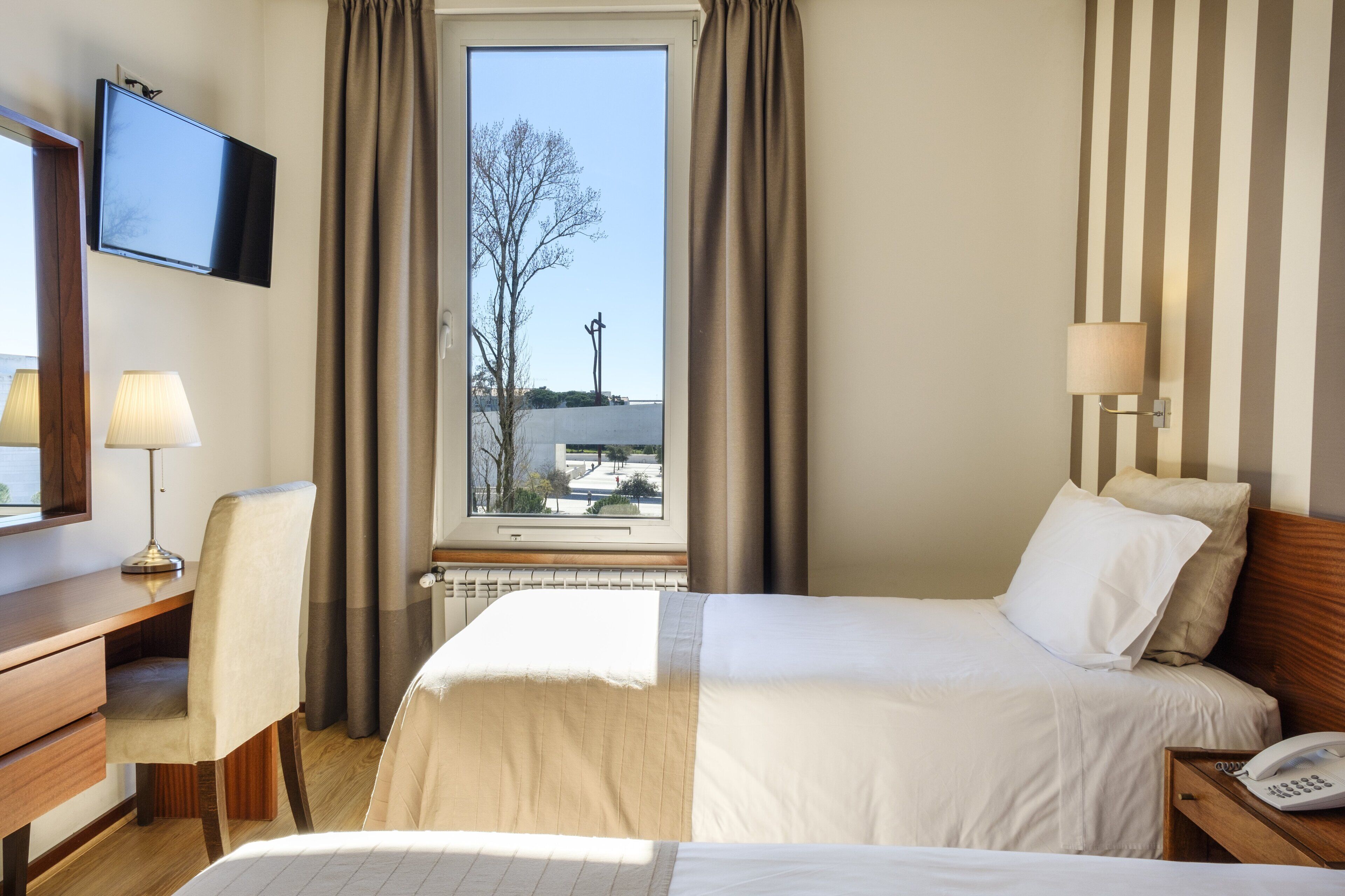 A hotel room with a bed, a desk, a chair, a TV, a lamp, and a window with curtains.