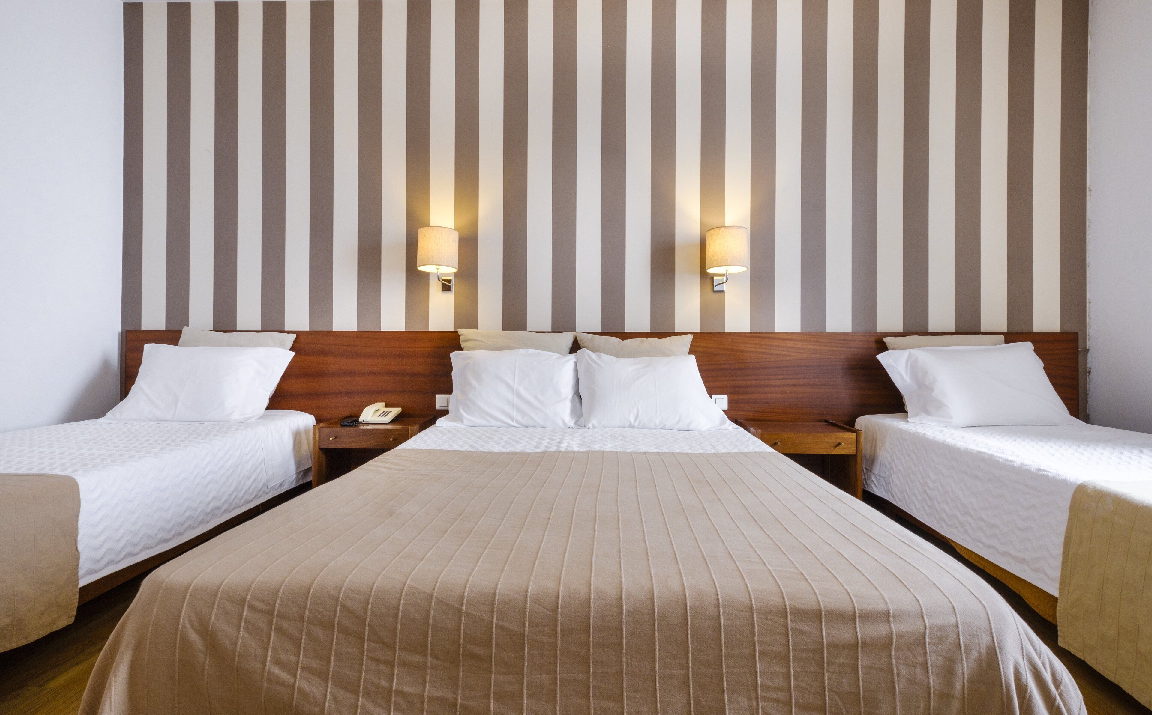 Quarto de hotel com uma cama grande, duas mesas de cabeceira e uma parede listrada.