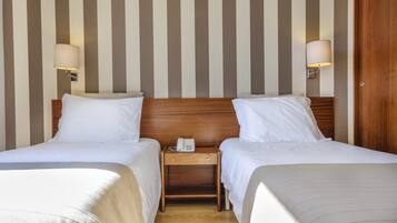 A hotel room with two beds, a wooden nightstand with a phone, and wall-mounted lamps.