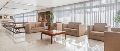 A spacious lobby with a high ceiling, a wooden staircase, and a large window with sheer curtains.