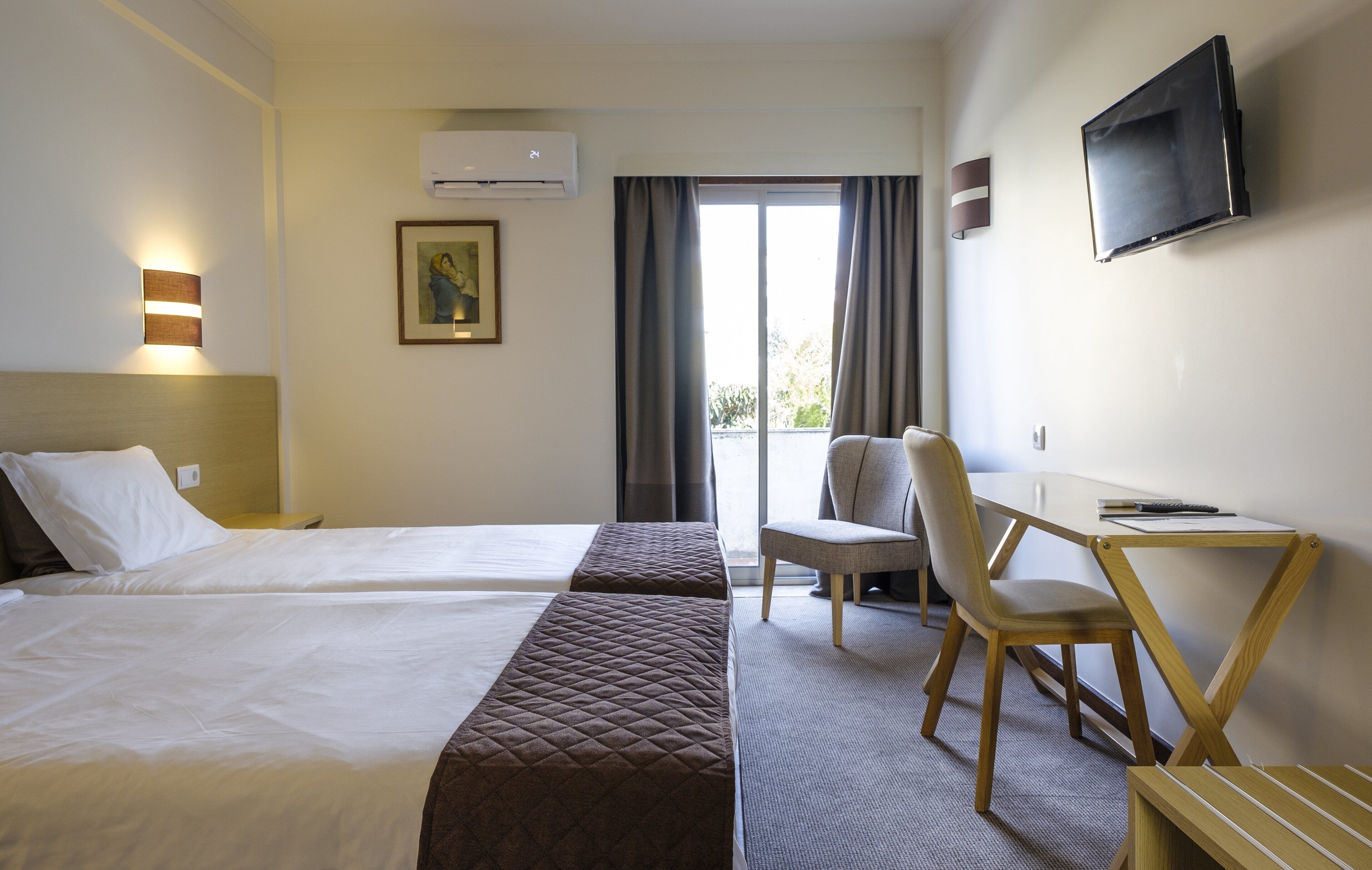 Une chambre d’hôtel avec deux lits, un bureau, une chaise, une télévision et une fenêtre avec des rideaux.