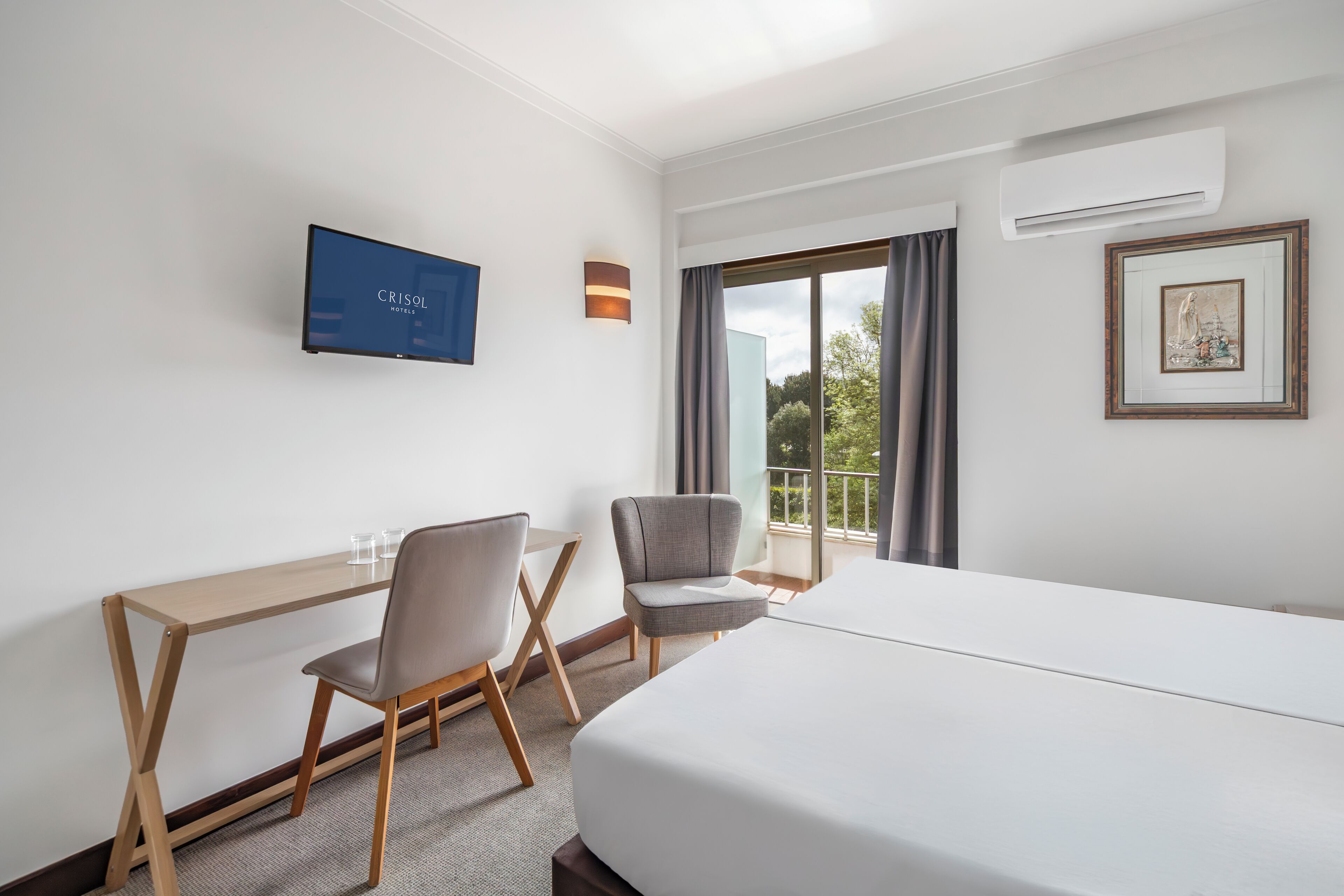 Habitación de hotel con cama, escritorio, dos sillas, televisor y balcón con vistas.