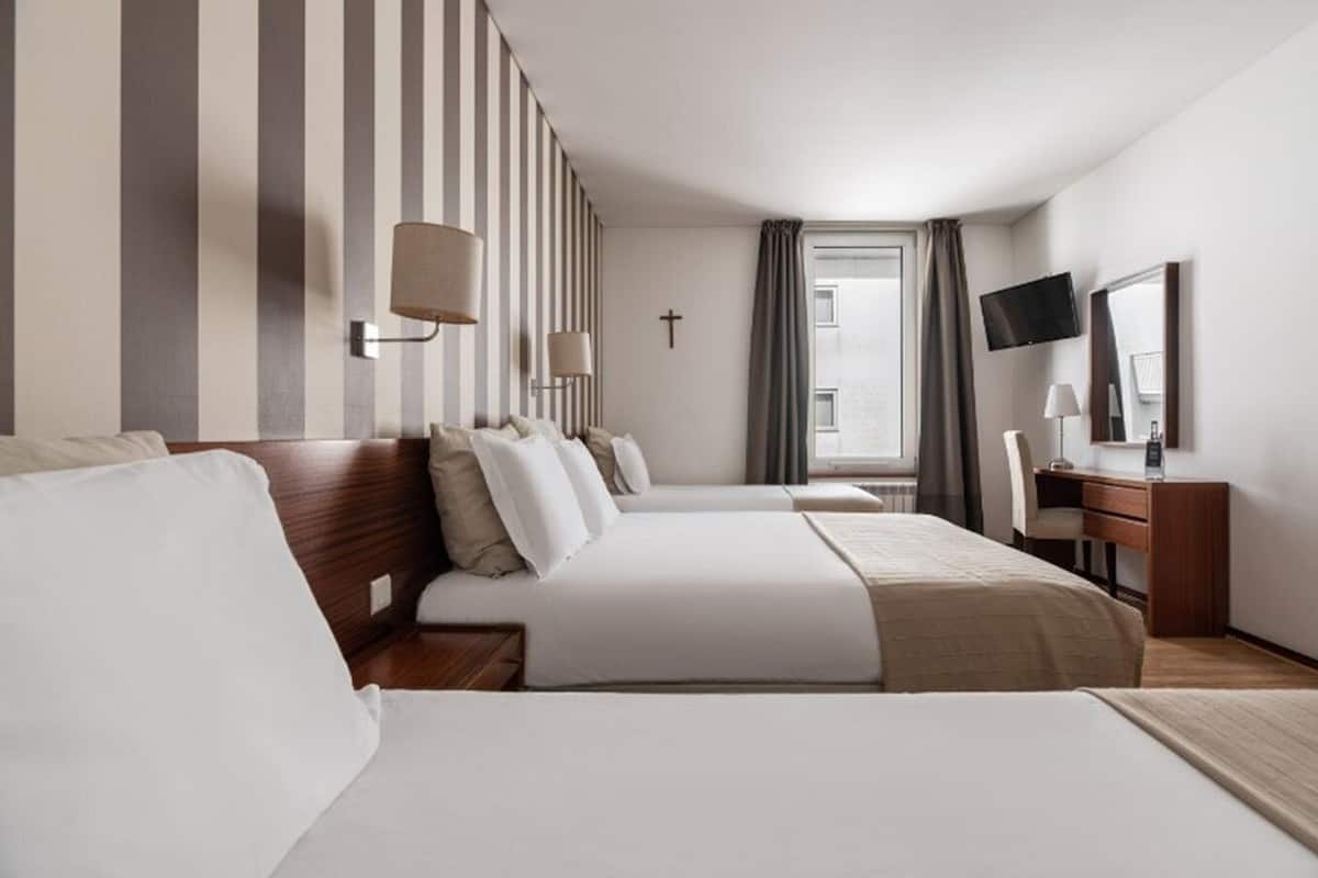 A hotel room with two beds, a desk, a TV, and a window with curtains.