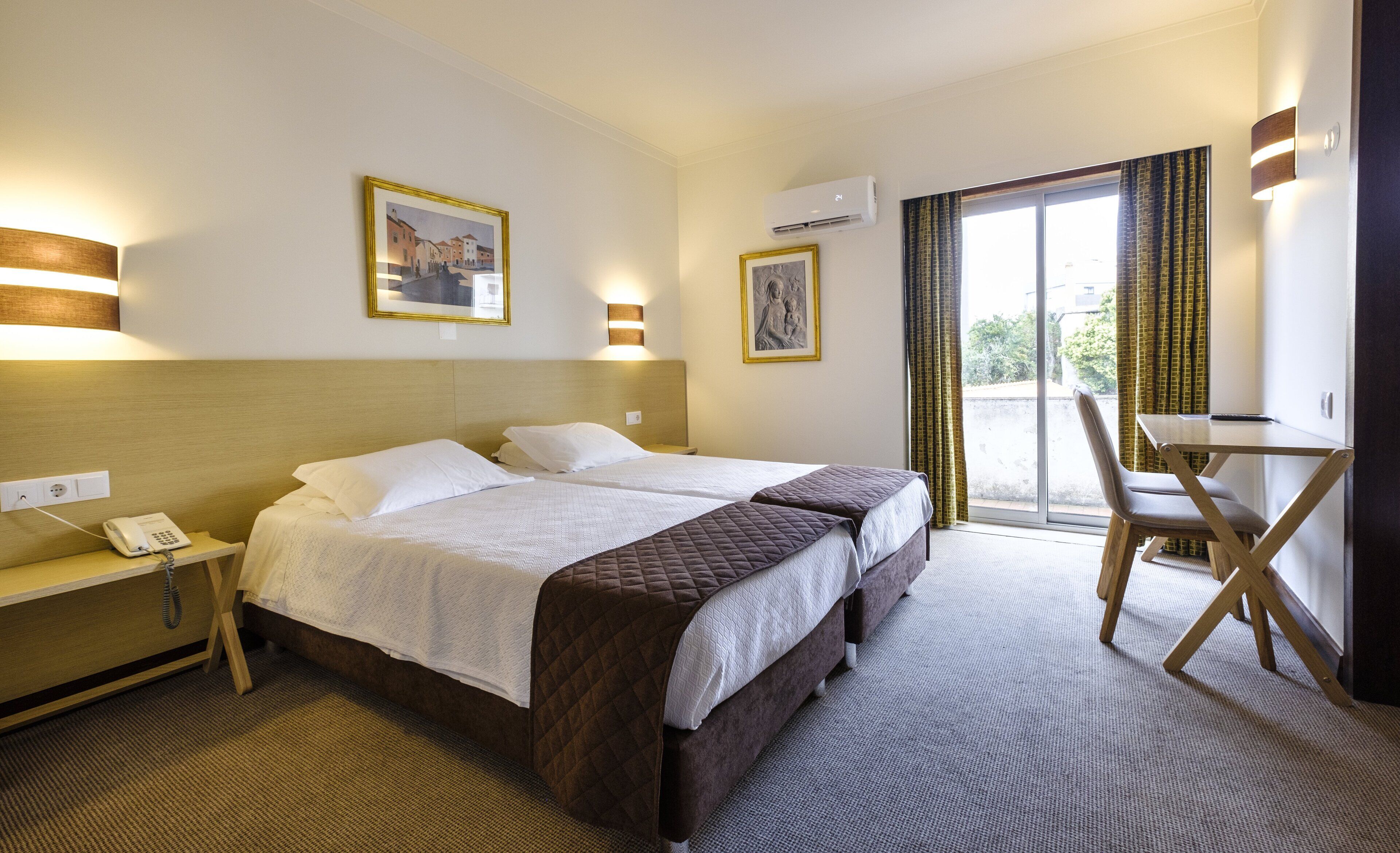 Ein Hotelzimmer mit zwei Betten, einem Schreibtisch, einem Stuhl, einem Telefon und Bildern an den Wänden.