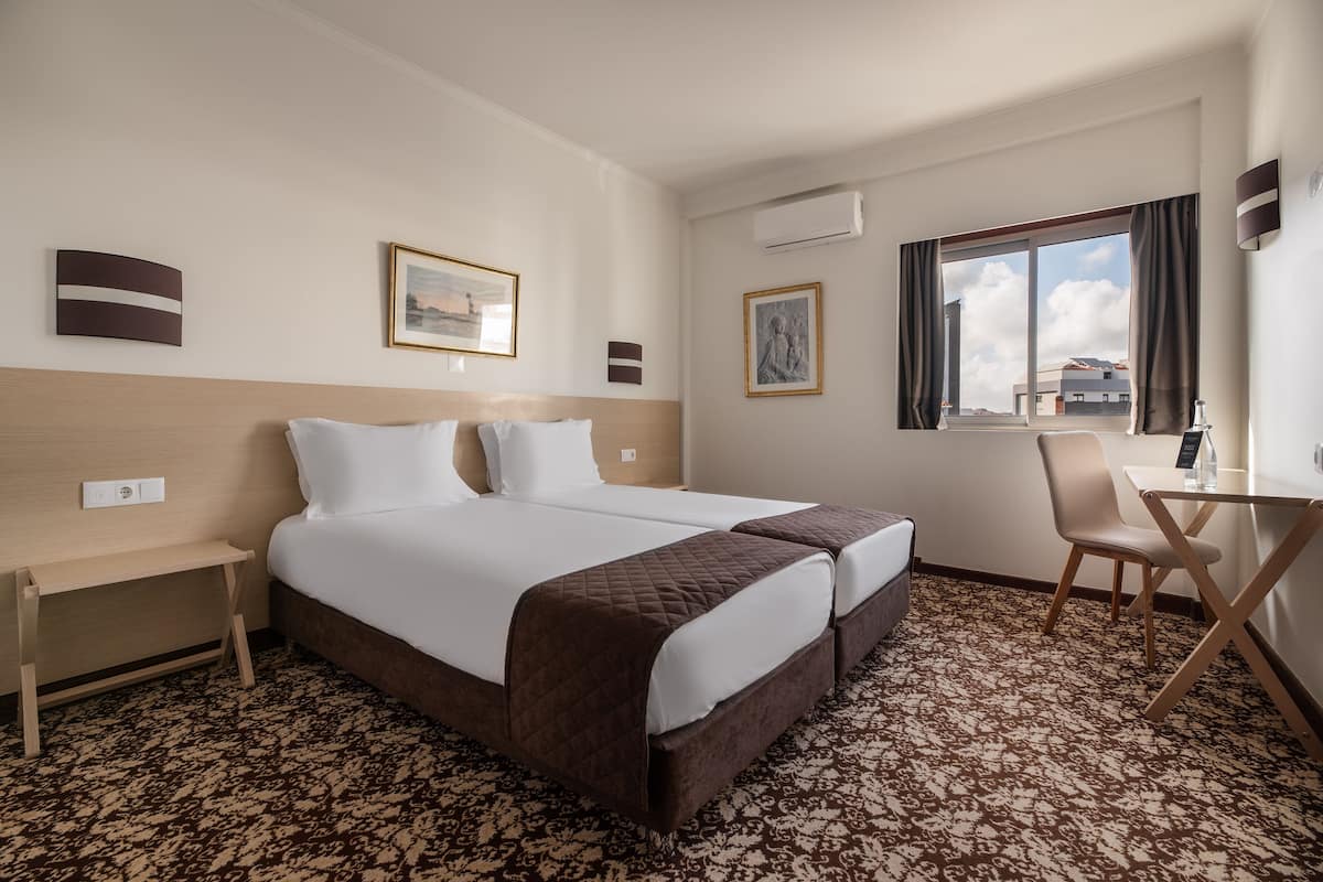 A hotel room with a large bed, a desk, a chair, and a window with curtains.
