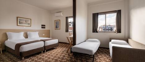 A hotel room with two beds, a small sofa, a window with curtains, and a patterned carpet.