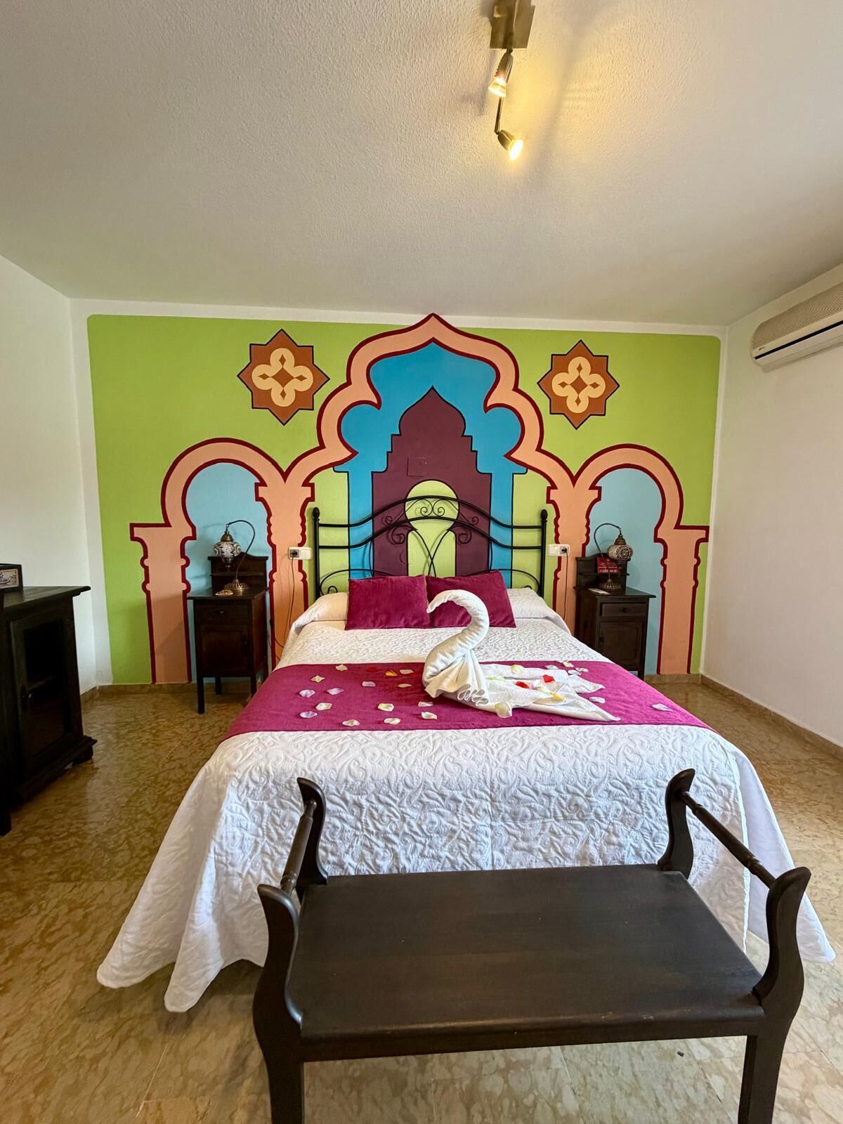 Una habitación de hotel con cama, mesita de noche, silla y un cabecero decorativo.