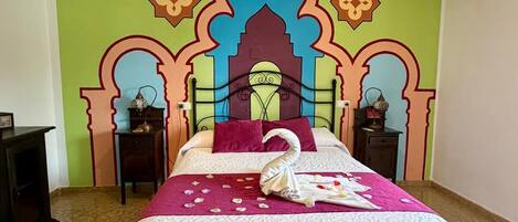 Una habitación de hotel con cama, mesita de noche, silla y un cabecero decorativo.