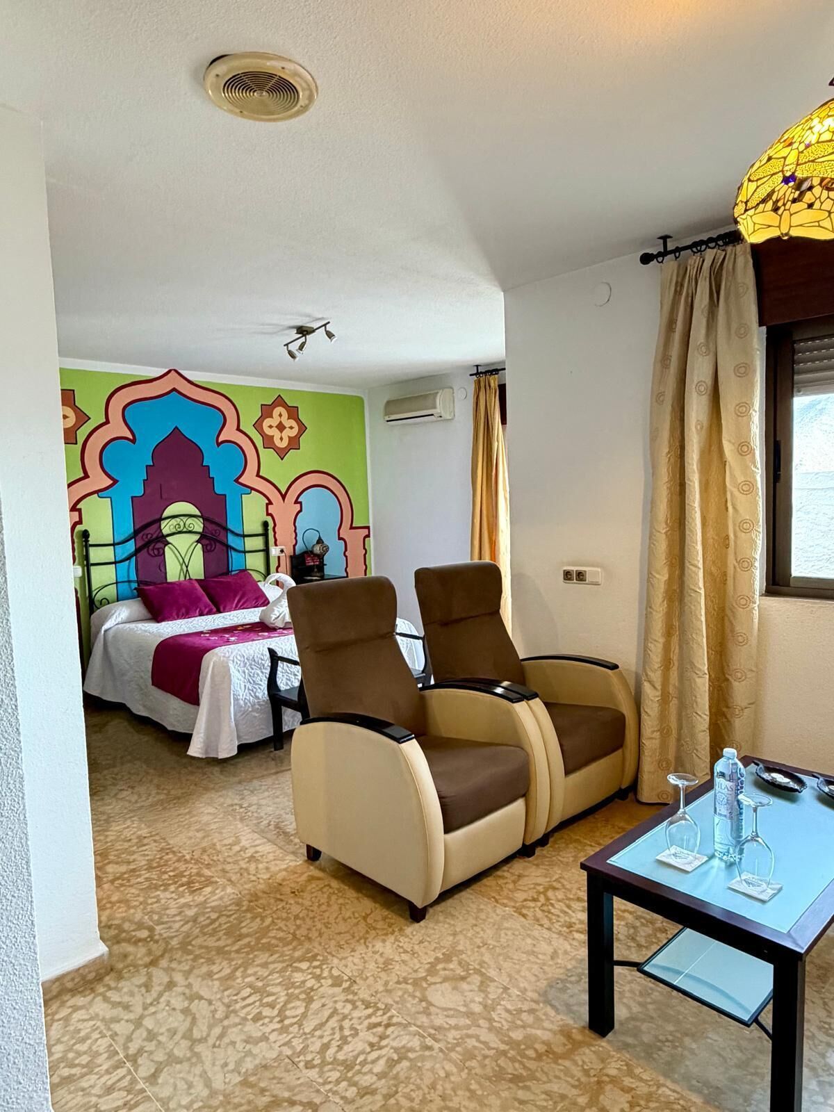 A hotel room with a bed, two armchairs, a small table, and a decorative wall mural.
