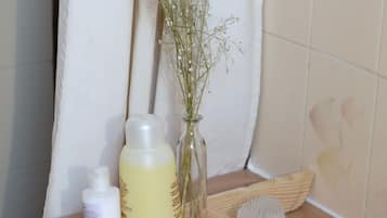 Un tocador de baño con artículos de aseo, un florero con flores y una toalla.