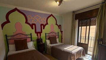 Habitación de hotel con dos camas, un adorno mural, una ventana con cortinas y un balcón.