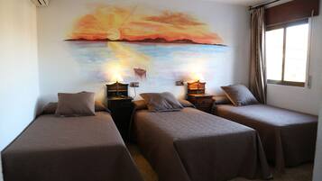Een kamer met twee eenpersoonsbedden, een nachtkastje met een lamp, een wanddecoratie van een zonsondergang en een raam met gordijnen.