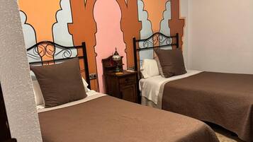 A hotel room with two beds, a nightstand with a lamp, and a decorative wall with geometric patterns.