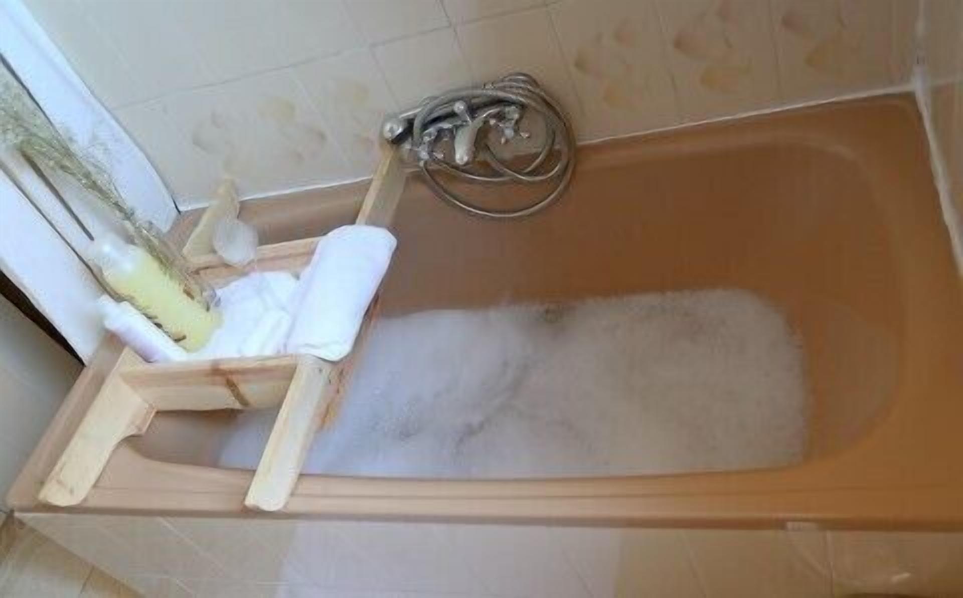 Una bañera con un lateral de madera, una toalla blanca y un grifo de metal.