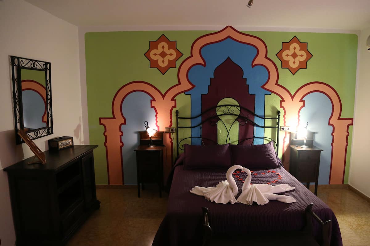 A bedroom with a bed, two bedside tables, a mirror, and a decorative wall with arches.