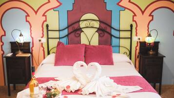 A bed with a heart-shaped towel arrangement, a bottle of wine, and a bouquet of flowers on a bedspread.