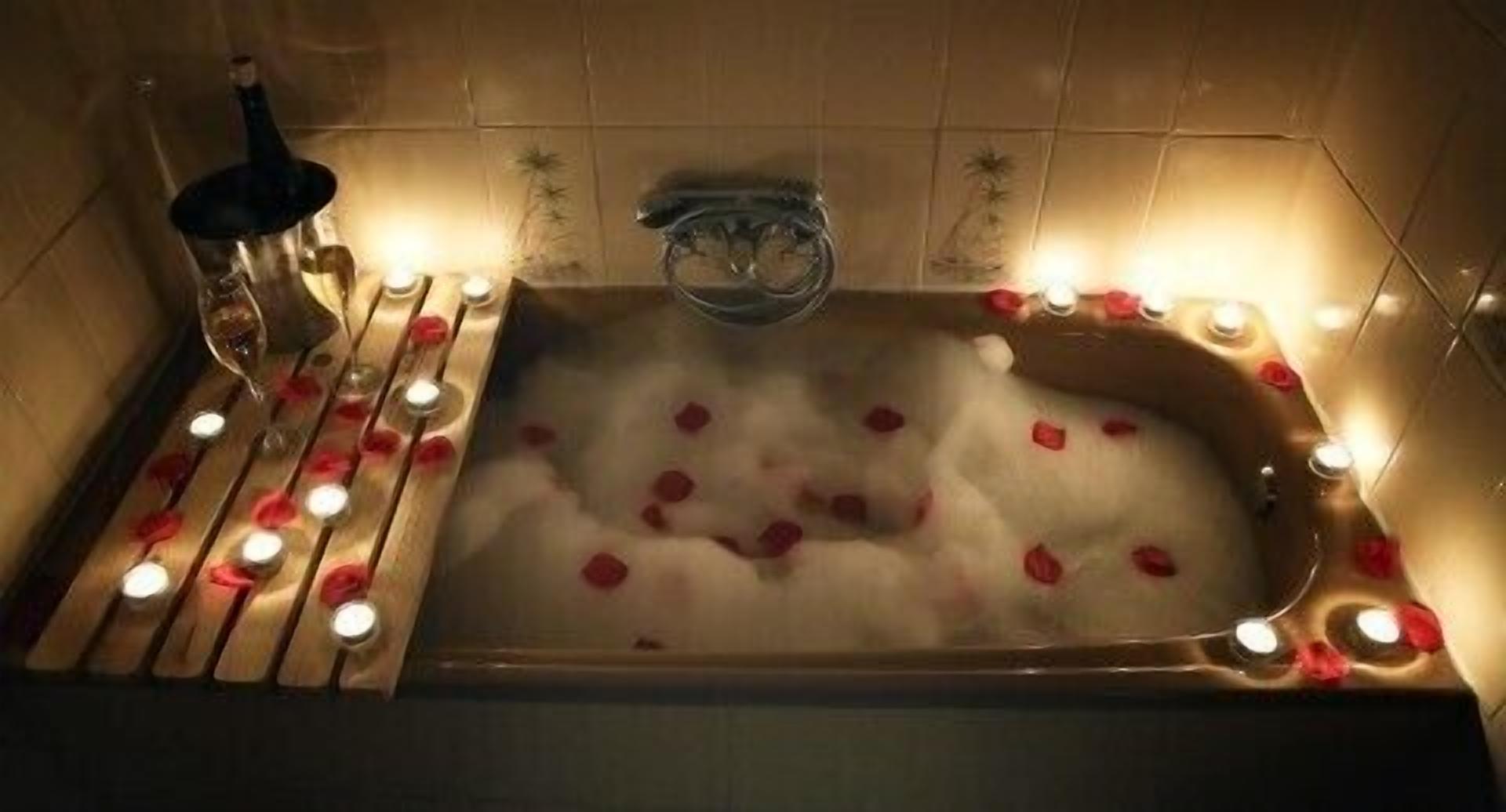 A bathtub with rose petals and candles.