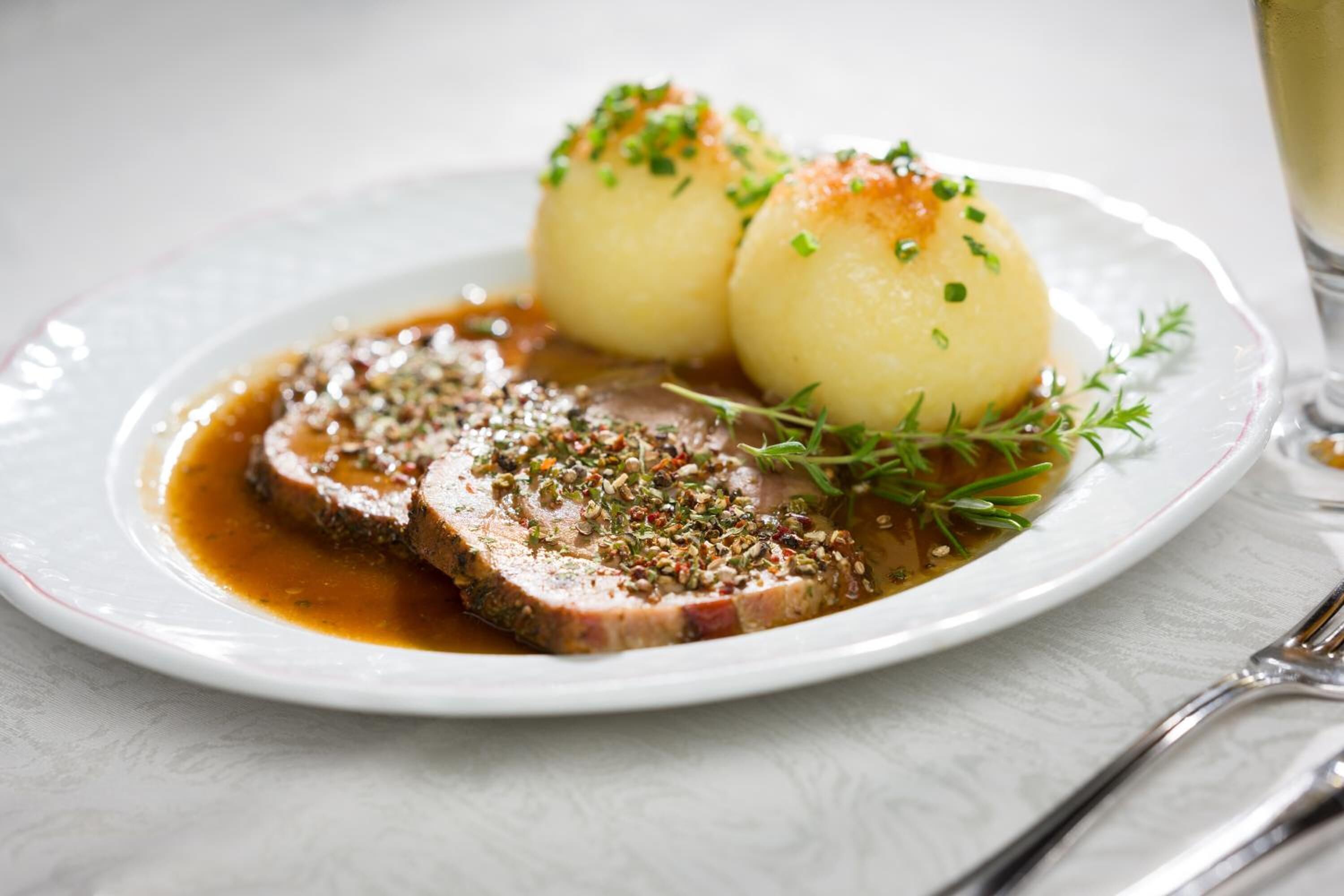 A plate with a slice of meat, two boiled potatoes, and a sprig of thyme.