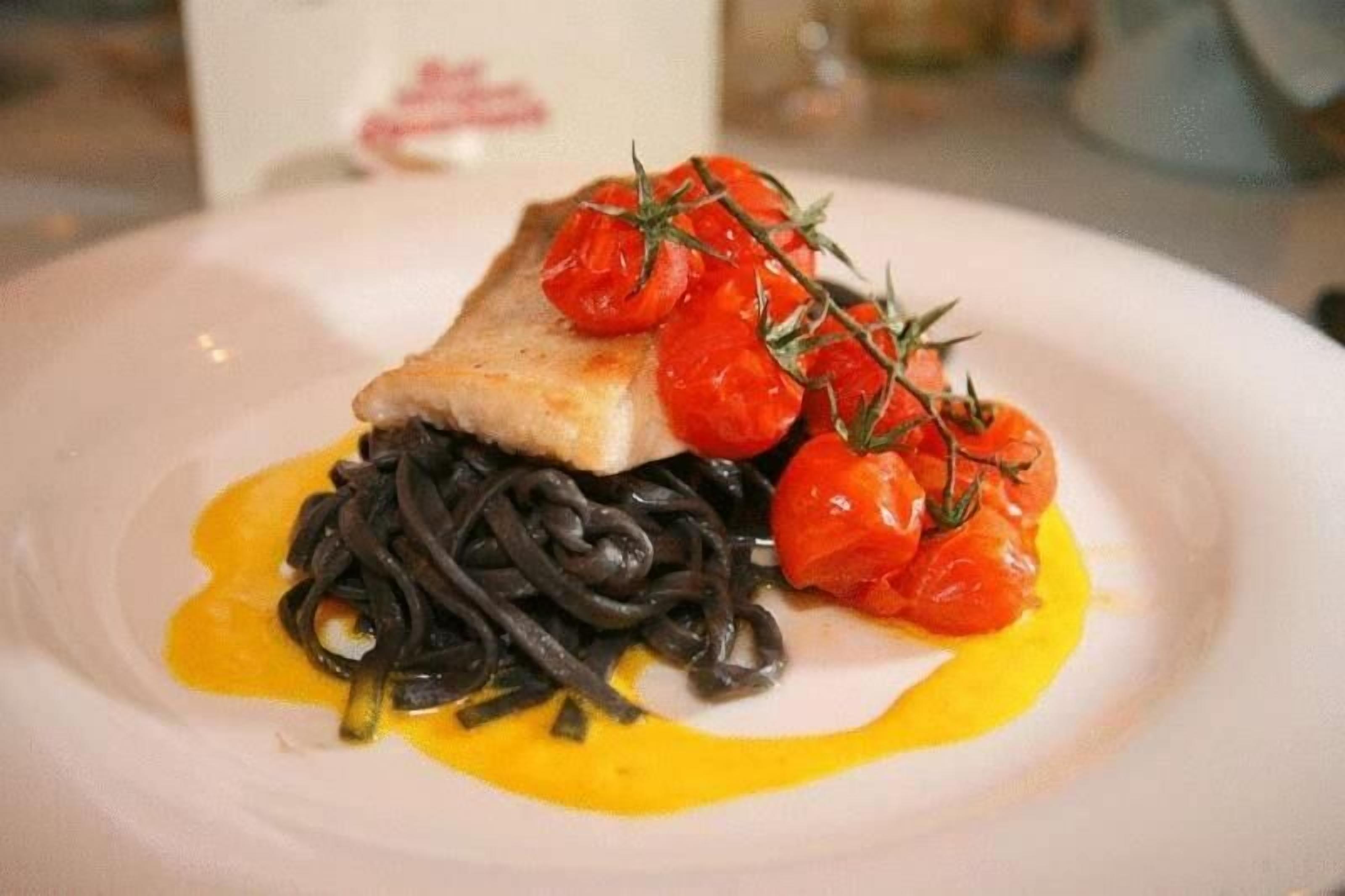 Un plato con un trozo de pescado, tomates cherry y una salsa amarilla.