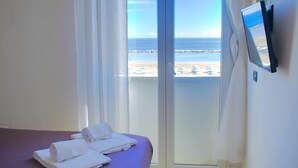 Habitación de hotel con cama, televisor en la pared y vista al mar a través de la ventana.