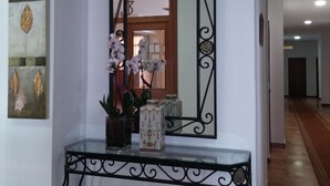 Um corredor com um espelho, um vaso de flores e um quadro na parede.