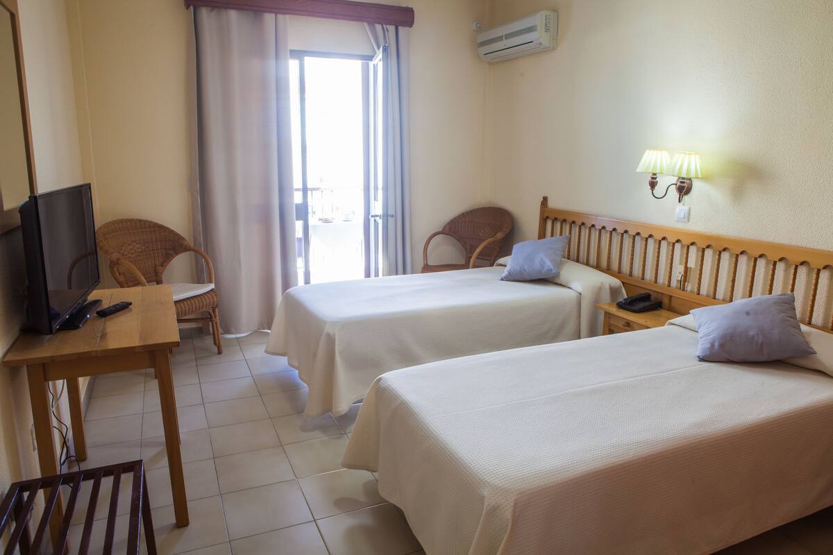 A hotel room with two beds, a television, a desk, and a chair.