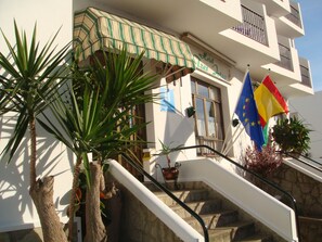 A hotel entrance with a staircase, a sign reading "Hotel Leros Jotas," and flags including the European Union flag. - Hotel Tres Jotas (Conil de la Frontera)