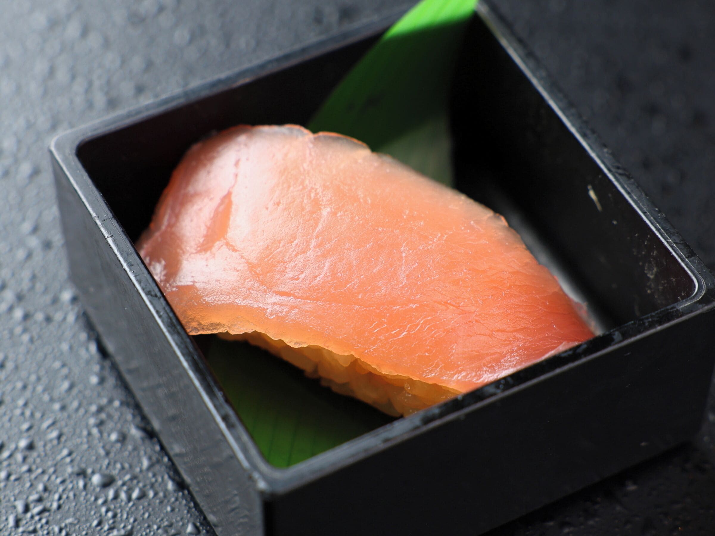 A rectangular black box containing a piece of salmon.