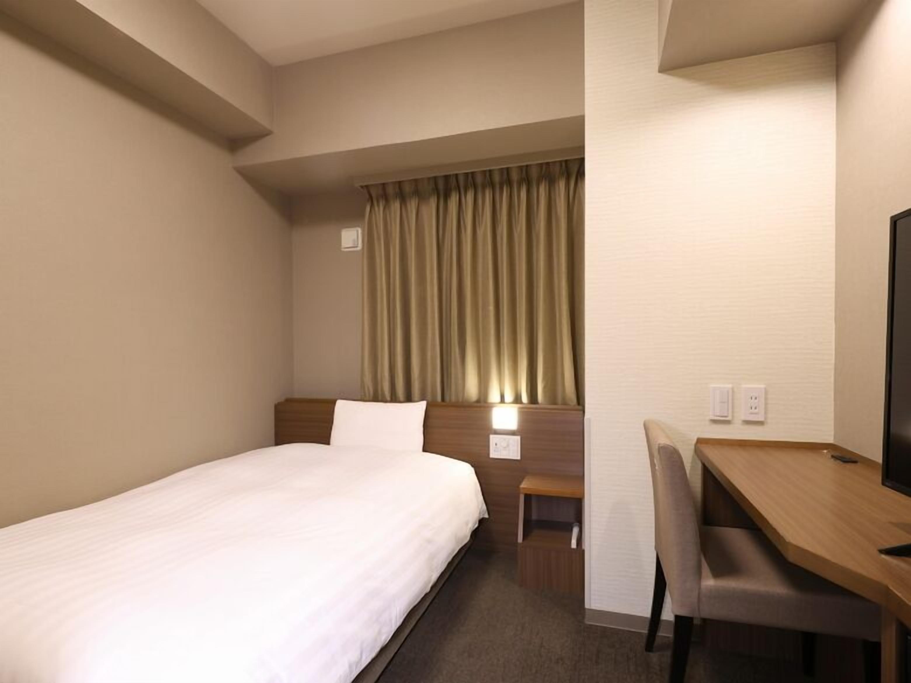 Une chambre d’hôtel équipée d’un lit, d’un bureau, d’une chaise, d’une télévision et d’une fenêtre avec des rideaux.