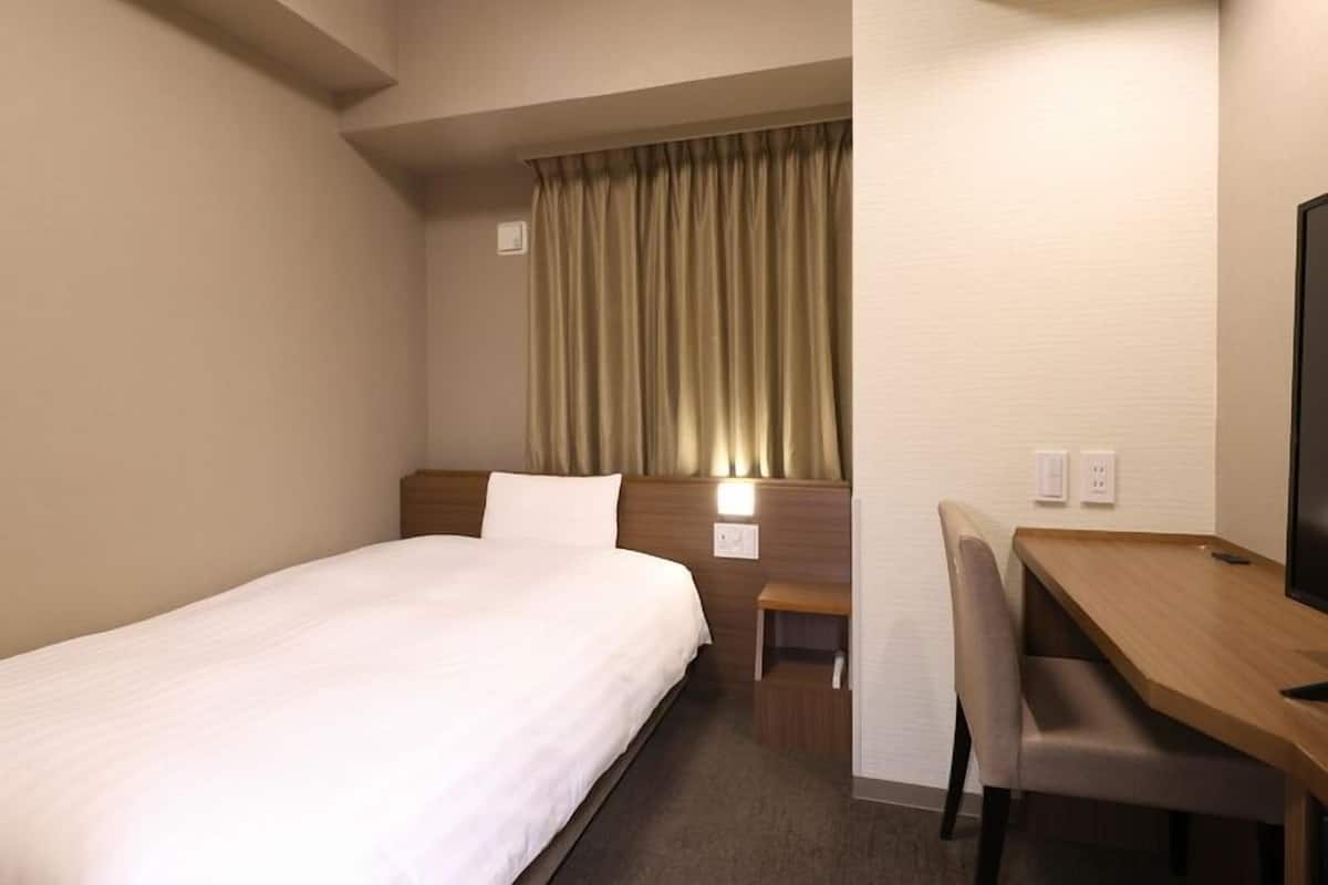 Une chambre d’hôtel équipée d’un lit, d’un bureau, d’une chaise, d’une télévision et d’une fenêtre avec des rideaux.